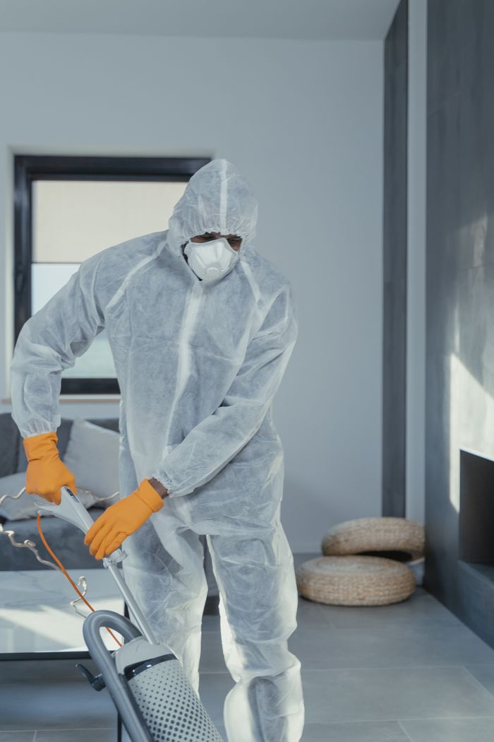 services-03 A person in personal protective equipment vacuuming indoors, ensuring a thorough clean.